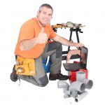 Man kneeling with laptop computer and plumbing tools